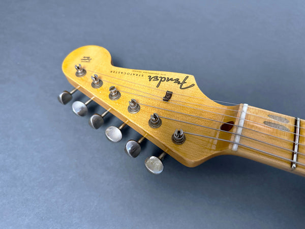 Close-up of vintage Fender Stratocaster guitar headstock with tuning pegs and strings on gray background