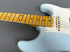 Close-up of light blue electric guitar body and maple fretboard with dot inlays on gray background, showing single-coil pickup and worn finish details