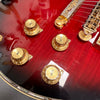 Close-up of red electric guitar body with gold volume and tone control knobs and chrome bridge hardware