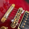 Close-up of red electric guitar bridge and tailpiece with gold hardware and six strings on Coffee House Guitars product listing