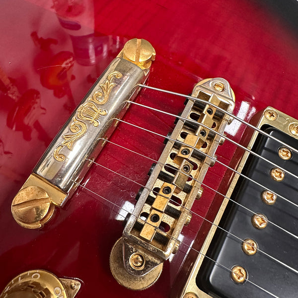 Close-up of red electric guitar bridge and tailpiece with gold hardware and six strings on Coffee House Guitars product listing