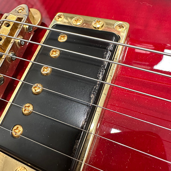 Close-up of red electric guitar with gold hardware and black pickup under steel strings showing wear on pickup edge