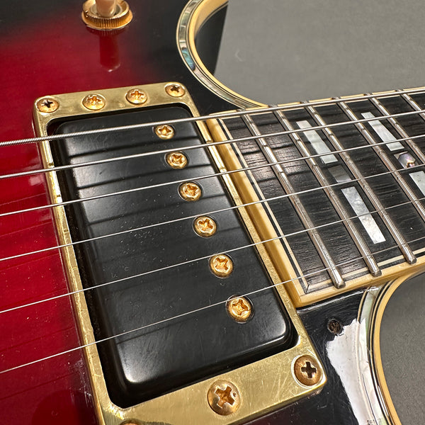 Close-up of electric guitar gold pickup and red sunburst body with pearl inlays on rosewood fretboard at Coffee House Guitars