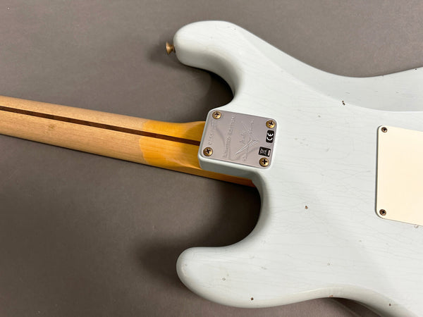 Close-up of the back of a white vintage electric guitar body and neck joint showing maple neck with skunk stripe and metal neck plate with serial number on a grey background.