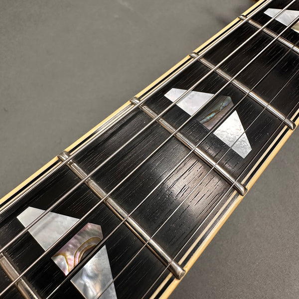 Close-up of guitar fretboard with mother of pearl inlays, metal frets, and steel strings on dark wood fingerboard with cream binding