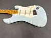 Vintage light blue electric guitar with maple neck and three single-coil pickups on gray background
