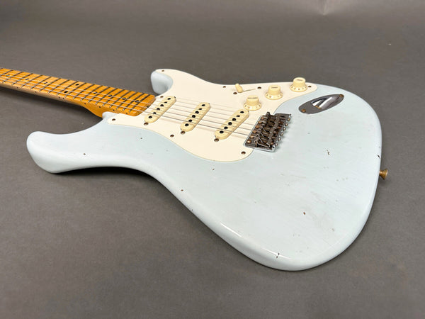 Light blue electric guitar with maple neck and white pickguard on gray background, vintage-style Stratocaster guitar body with three single-coil pickups and volume and tone control knobs