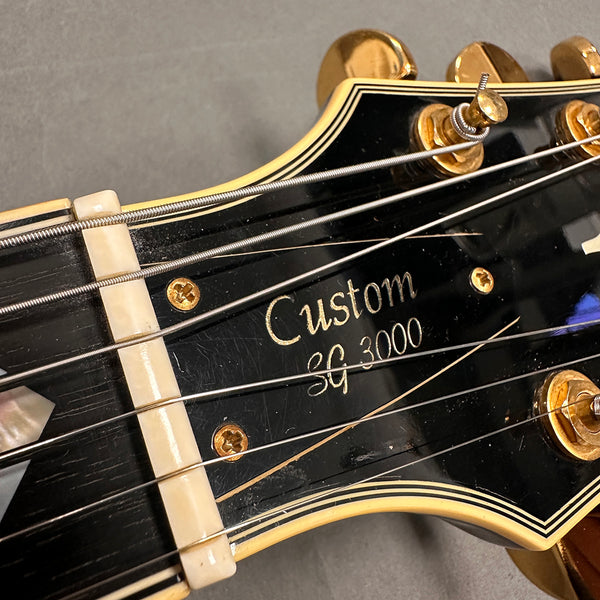 Close-up of Custom SG 3000 guitar headstock with gold tuning pegs and black finish