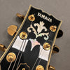 Close-up of Yamaha acoustic guitar headstock with mother of pearl inlay and gold tuning pegs on gray background