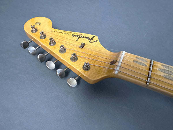 Close-up of vintage Fender Stratocaster electric guitar maple neck and headstock with tuning pegs and strings on gray background