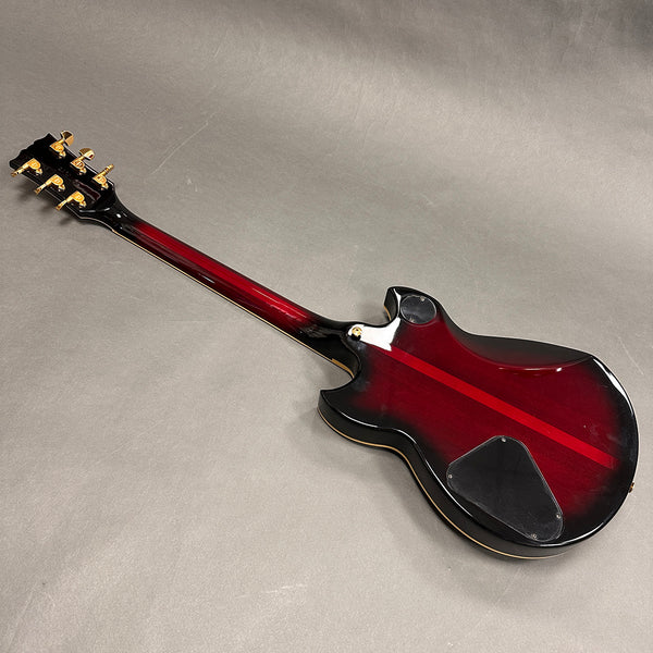 Back view of red and black electric guitar with gold tuning pegs on gray background