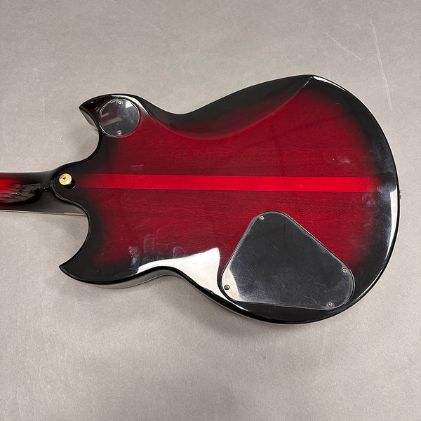 Back view of red and black electric guitar body with control cavity plate and strap button on gray background