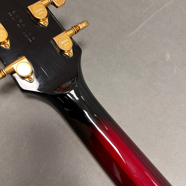 Close-up of Yamaha guitar neck and headstock showing tuning pegs and serial number made in Japan, glossy black to red sunburst finish guitar neck.