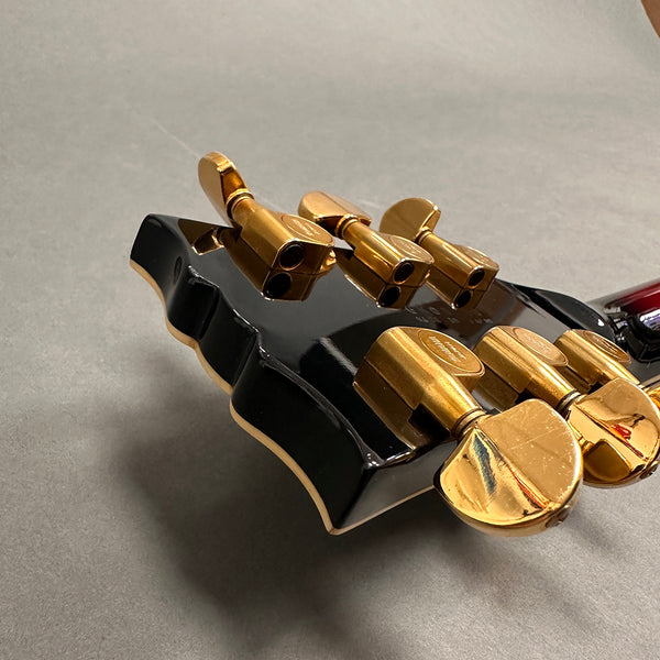 Close-up of black guitar headstock with gold tuning pegs on gray background