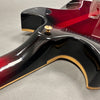 Close-up of guitar neck joint and strap button on red and black electric guitar with cream binding on gray surface