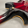 Close-up of black and red electric guitar body with gold trim and strap button on gray surface