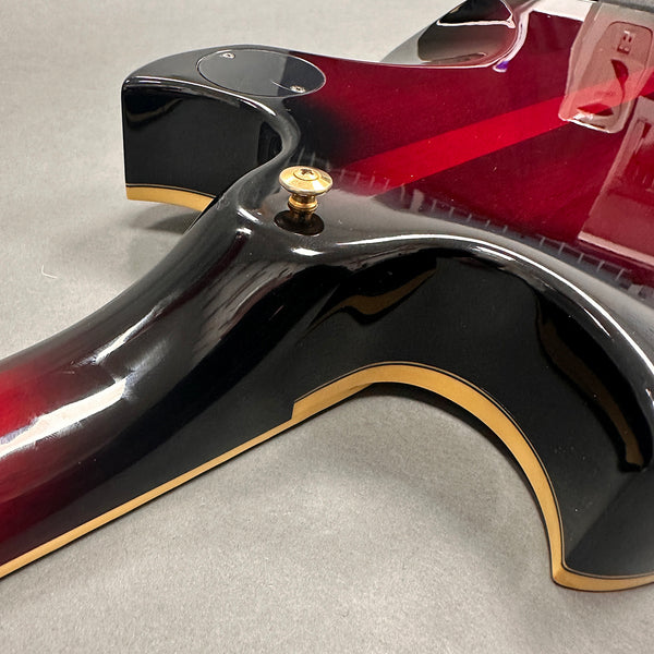 Close-up of black and red electric guitar body with gold trim and strap button on gray surface