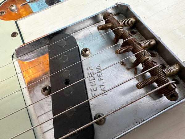 Close-up image of vintage Fender Telecaster bridge and single-coil pickup with strings and adjustable saddles showing wear and patina