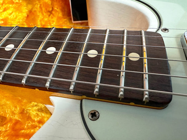 Close-up of electric guitar fretboard with metal frets, dot inlays, and strings on a white body guitar with yellow plush background