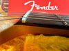 Close-up of acoustic guitar nut and strings with red Fender logo background and yellow plush guitar case lining
