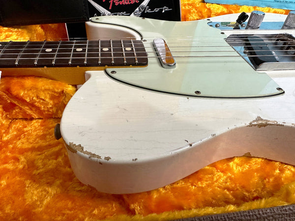 Close-up of vintage white Fender Telecaster electric guitar body with worn paint and visible wood chips, resting on bright orange plush guitar case lining, featuring rosewood fretboard and metal pickups.