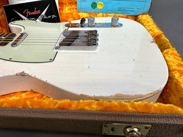 Close-up of vintage white Fender Telecaster guitar body with visible wear and paint chipping, displayed in a yellow plush-lined hardshell case with Fender Custom Shop paperwork in the background.