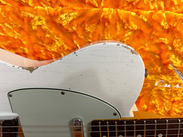 Close-up of vintage white electric guitar body with worn edges and cream pickguard on orange plush case lining with visible guitar strings and fretboard