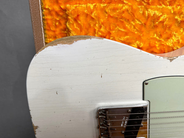 Close-up of vintage white electric guitar body with worn edges and aged finish, showcasing metal bridge and pickup, partially resting on orange plush-lined guitar case