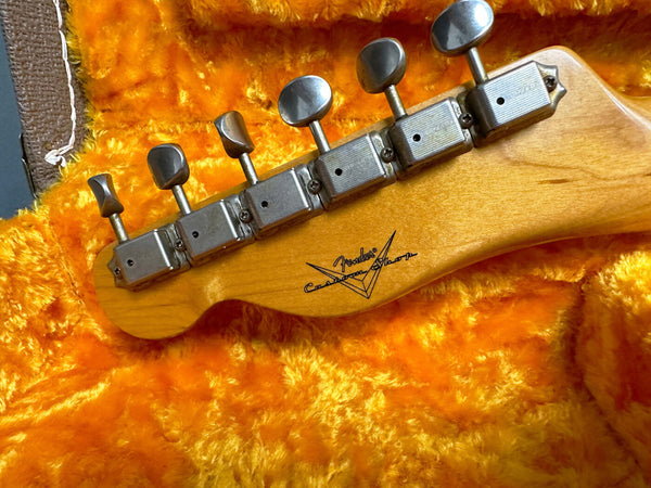 Vintage Fender Custom Shop guitar headstock with six tuning pegs resting on bright orange plush guitar case lining