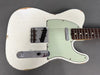Vintage white Fender Telecaster electric guitar with worn finish, mint green pickguard, and rosewood fingerboard, shown from front angle on gray background