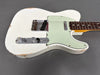 Close-up of vintage white electric guitar with mint green pickguard and worn body finish showing chrome knobs and bridge on gray background