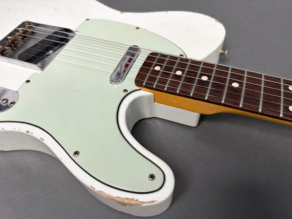 Close-up of a vintage white electric guitar body with light wear and scratches, showing the greenish pickguard, single-coil pickups, and rosewood fretboard with dot inlays on a gray background