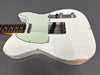 White electric guitar with worn finish and mint green pickguard, showing vintage style single-coil pickups and chrome control knobs on gray background
