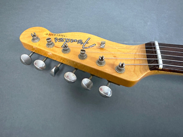 Close-up of a Fender Telecaster electric guitar headstock with tuning pegs and strings on a gray background