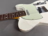 Close-up of vintage white electric guitar body and rosewood fretboard with wear and chipped paint on guitar edges, chrome bridge and control knobs on gray background.