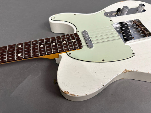 Close-up of vintage white electric guitar body and rosewood fretboard with wear and chipped paint on guitar edges, chrome bridge and control knobs on gray background.