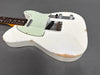 Close-up of vintage white Fender Telecaster electric guitar body with worn edges and greenish pickguard on gray background