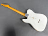 Back of vintage white electric guitar with maple neck and metal neck plate showing worn finish and string ferrules on gray background