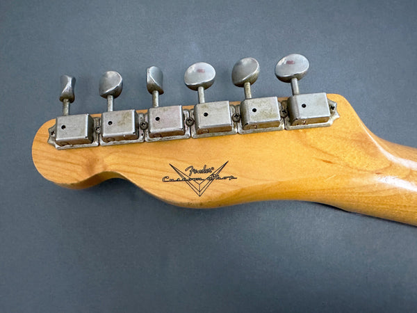 Close-up of vintage Fender Custom Shop guitar headstock with six metal tuning pegs on natural wood finish against dark background