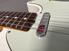 Close-up of vintage electric guitar bridge and rosewood fingerboard with white dot inlays on light green guitar body.