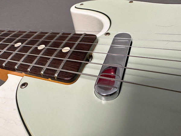 Close-up of vintage electric guitar bridge and rosewood fingerboard with white dot inlays on light green guitar body.