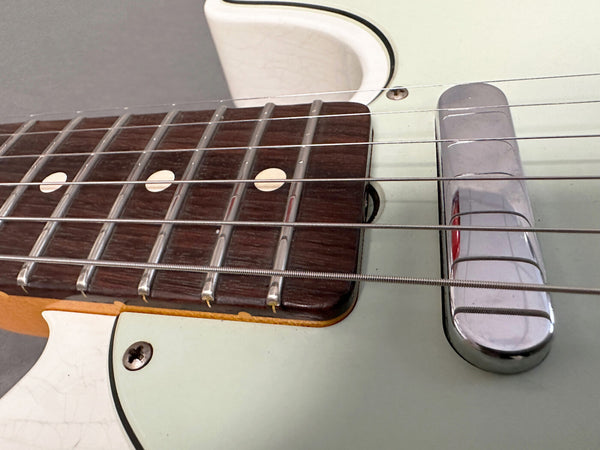 Close-up of electric guitar fretboard and chrome pickup cover with metal strings and dot inlays on dark wood fingerboard