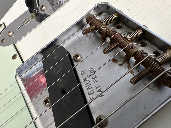 Close-up of vintage Fender guitar bridge and single-coil pickup with visible Fender patent stamp and aged metal parts