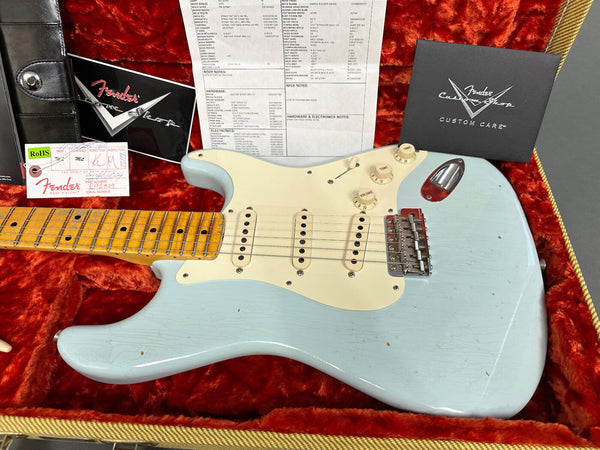 Fender Custom Shop electric guitar in light blue finish with maple neck and aged white pickguard, displayed in orange plush-lined hard case with Fender Custom Shop documentation and tags
