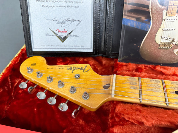 Close-up of Fender Stratocaster maple neck headstock with tuning pegs, certificate of authenticity from Fender Custom Shop, and red plush guitar case interior.