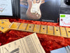 Close-up of vintage Fender guitar maple neck and frets on red plush case lining with Fender instruction manual and certificate in background
