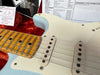 Close-up of vintage Fender Stratocaster electric guitar pickups, maple fretboard with aged wear, and official guitar inspection and specification documents on a red plush case lining.