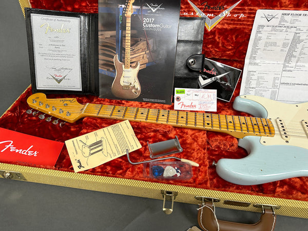 Fender Stratocaster guitar in light blue with vintage-style tweed case lined with orange plush, including Fender certificate of authenticity, 2017 Custom Guitar design guide, owner's manual, pick set, tremolo spring guide, and Fender shop floor tracking sheet.