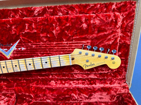 Fender Stratocaster guitar headstock with maple neck and vintage tuners on red plush case lining