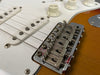 Close-up of Fender electric guitar chrome bridge, strings, white volume and tone knobs, and sunburst finish body